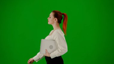 Modern iş kadını yaratıcı reklam konsepti. Krom anahtar yeşil ekranda çekici ofis kızı portresi. Etekli ve bluzlu bir kadın elinde dizüstü bilgisayarla yürüyor. Yan görünüm.