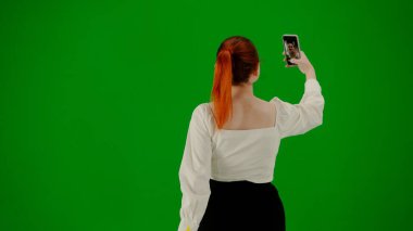 Modern iş kadını yaratıcı reklam konsepti. Krom anahtar yeşil ekranda çekici ofis kızı portresi. Etek giyen bir kadın akıllı telefondan selfie çekiyor. Arka plan.