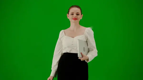 Modern business woman creative advertisement concept. Portrait of attractive office girl on chroma key green screen. Woman in skirt and blouse walking holding laptop, looking at the camera smiling.