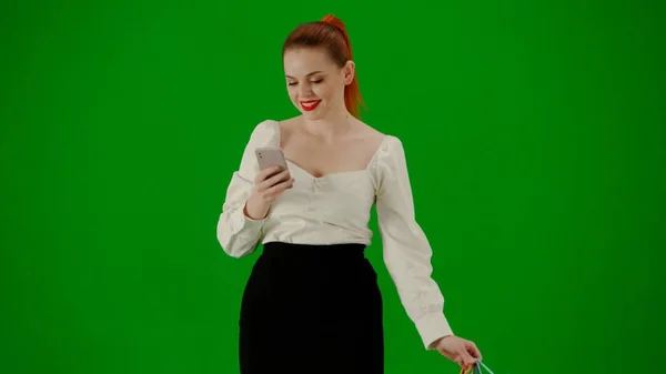 現代のビジネス女性クリエイティブ広告コンセプト クロマキーグリーンスクリーンの魅力的なオフィスガールの肖像画 スカートで歩く女性 ギフトバッグを保持し スマートフォンでテキスト — ストック写真