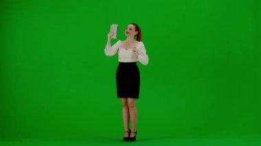 Modern iş kadını yaratıcı reklam konsepti. Krom anahtar yeşil ekranda çekici ofis kızı portresi. Etekli ve bluzlu kadın tabletten video çağrısı ile konuşuyor, olumlu ifade..