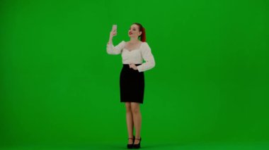 Modern iş kadını. Krom anahtar yeşil ekranda çekici ofis kızı portresi. Etekli ve bluzlu kadın cep telefonuyla video görüşmesiyle konuşuyor, olumlu ifade.