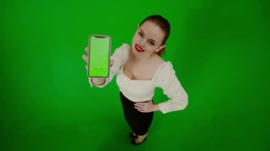 Modern iş kadını yaratıcı reklam konsepti. Krom anahtar yeşil ekranda çekici ofis kızı portresi. Kameraya telefonu gösteren akıllı telefonu tutan, gülümseyen bir kadın..