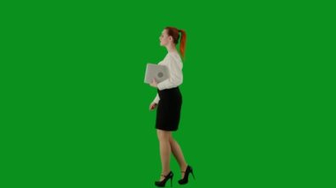 Modern iş kadını yaratıcı reklam konsepti. Krom anahtar yeşil ekranda çekici ofis kızı portresi. Etekli ve bluzlu bir kadın elinde dizüstü bilgisayarla yürüyor. Yan görünüm.