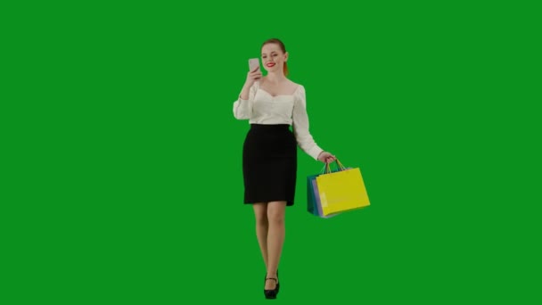 現代のビジネス女性クリエイティブ広告コンセプト クロマキーグリーンスクリーンの魅力的なオフィスガールの肖像画 スマートフォンでセルフィーを取るギフトバッグを持って歩くスカートの女性 — ストック動画