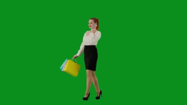 現代のビジネス女性 クロマキーグリーンスクリーンの魅力的なオフィスガールの肖像画 スカートの女性はギフトバッグを持って歩き スマートフォンで笑顔で話します ハーフターン — ストック動画