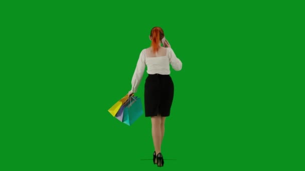 現代のビジネス女性クリエイティブ広告コンセプト クロマキーグリーンスクリーンの魅力的なオフィスガールの肖像画 スカートの女性はギフトバッグを持って歩き スマートフォンで話します バックビュー — ストック動画