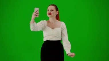 Modern iş kadını yaratıcı reklam konsepti. Krom anahtar yeşil ekranda çekici ofis kızı portresi. Etekli bir kadın yürüyor ve akıllı telefondan selfie çekiyor, gülümsüyor..