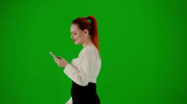 Modern iş kadını yaratıcı reklam konsepti. Krom anahtar yeşil ekranda çekici ofis kızı portresi. Etekli bir kadın elinde hediye çantalarıyla yürüyüp akıllı telefondan mesaj atıyor. Yan görünüm.