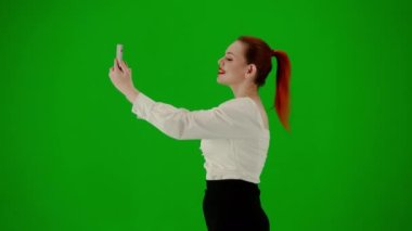 Modern iş kadını yaratıcı reklam konsepti. Krom anahtar yeşil ekranda çekici ofis kızı portresi. Etek giyen bir kadın akıllı telefondan selfie çekiyor. Yan görünüm.
