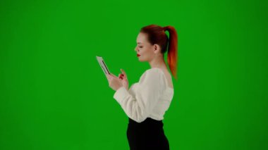 Modern iş kadını yaratıcı reklam konsepti. Krom anahtar yeşil ekranda çekici ofis kızı portresi. Etekli ve bluzlu bir kadın elinde tabletle yürüyor. Yan görünüm.