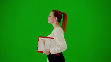 Modern iş kadını yaratıcı reklam konsepti. Krom anahtar yeşil ekranda çekici ofis kızı portresi. Etekli ve bluzlu bir kadın kırmızı klasör tutarak yürüyor. Yan görünüm.