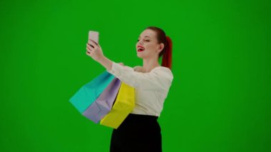 Modern iş kadını. Krom anahtar yeşil ekranda çekici ofis kızı portresi. Etek giyen, elinde hediye çantalarıyla gezen, akıllı telefondan selfie çeken, gülümseyen yüzlü bir kadın. Yarım dönüş..