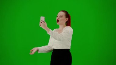 Modern iş kadını yaratıcı reklam konsepti. Krom anahtar yeşil ekranda çekici ofis kızı portresi. Etekli bir kadın yürüyor ve akıllı telefondan selfie çekiyor, gülümsüyor. Yarım dönüş..