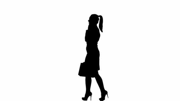 現代のビジネス女性 白い隔離された背景にオフィスの女の子の黒いシルエット スカートとブラウスの女性は 手のパッケージで歩き スマートフォンで話します サイドビュー — ストック動画