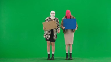 Kar maskeli ve sahte kürklü iki kadın yeşil ekranda stüdyoda grev yapıyorlar. Kadınlar ellerindeki afişleri ve afişleri göstererek slogan atıyorlar.