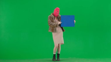 Pembe kar maskeli kadın, kaplan ceketli ve elinde mavi bayrak olan gece elbisesi. Stüdyoda yeşil arka plandaki ucube kadın. Moda eğilimi, feminist moda eğilimi
