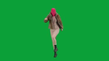 Pembe kar maskeli, kaplan kürklü ve gece elbisesi giymiş bir kadın dans edip zıplıyor. Stüdyoda yeşil arka plandaki ucube kadın. Moda eğilimleri kavramı, feminist moda eğilimi