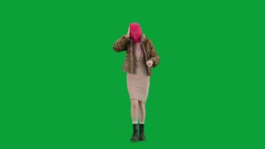 Pembe kar maskeli kadın, kaplan ceketli ve gece elbisesi giymiş. Stüdyoda yeşil arka plandaki ucube kadın. Moda eğilimleri kavramı, feminist moda eğilimi