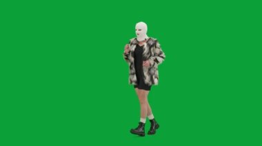 Beyaz kar maskeli kadın, palto ve gece elbisesi giyiyor. Stüdyoda yeşil arka plandaki ucube kadın. Moda eğilimleri, feminist moda eğilimi Yarım dönüş.