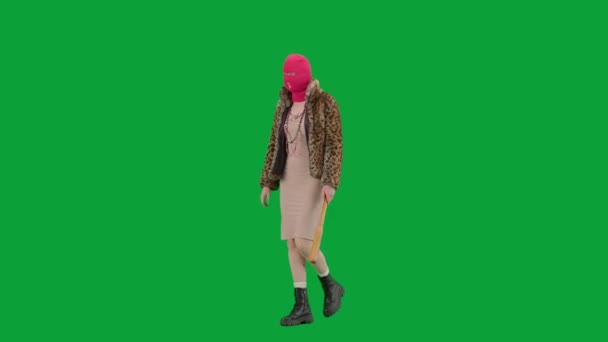 身穿粉色巴拉克拉瓦的女人 身穿虎皮大衣 身穿晚礼服 手里拿着球棒走路 工作室里的女性对绿色背景非常好奇 时尚潮流理念 女权主义潮流在时尚半圈 — 图库视频影像