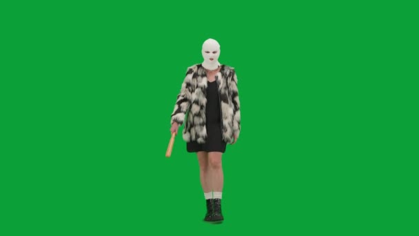 身穿白色巴拉克拉法帽 皮大衣和晚礼服的女人手拿着球棒走着 工作室里的女性对绿色背景非常好奇 时尚潮流的概念 时尚中的女权主义趋势 — 图库视频影像
