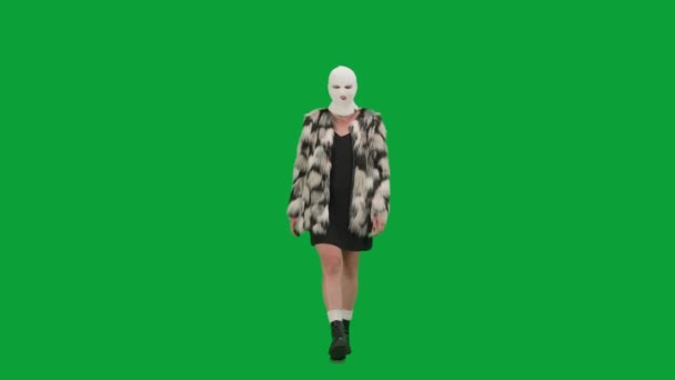 身穿白色巴拉克拉法帽 皮大衣和晚礼服的女人走路 工作室里的女性对绿色背景非常好奇 时尚潮流的概念 时尚中的女权主义趋势 — 图库视频影像