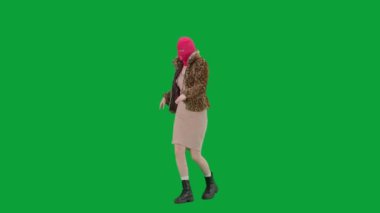Pembe kar maskeli, kaplan kürklü ve gece elbisesi giymiş bir kadın dans edip zıplıyor. Stüdyoda yeşil arka plandaki ucube kadın. Moda eğilimleri, feminist moda eğilimi Yarım dönüş.