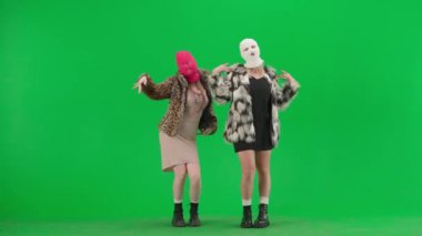 Beyaz ve pembe kar maskeli iki kadın seksi dans ediyor. Yeşil stüdyo arka planında kürk giyen ucube kadınlar. Moda eğilimi, feminist moda eğilimi