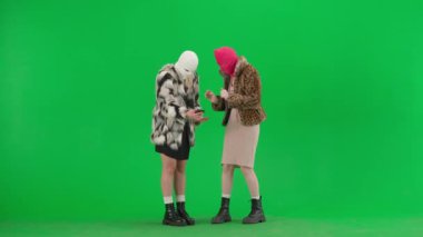 Beyaz ve pembe kar maskeli iki kadın akıllı telefona umutla bakıyor ve bir kayıp ya da kötü haber yüzünden üzülüyorlar. Stüdyonun yeşil arka planında kürk giyen kadınlar.