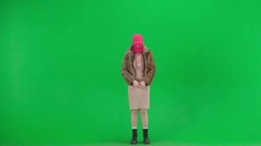 Pembe kar maskeli kadın, kaplan ceketli ve gece elbisesi sallanan ve kollarını sallayan. Stüdyoda yeşil arka plandaki ucube kadın. Moda eğilimi, feminist moda eğilimi