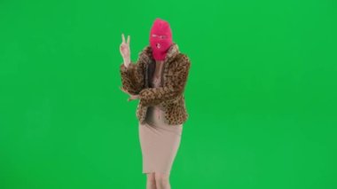 Pembe kar maskeli kadın, kaplan ceketli ve gece elbisesi giyen kadın zafer jesti gösteriyor. Stüdyoda yeşil bir geçmişi olan ucube bir kadın. Moda eğilimi, feminist moda eğilimi