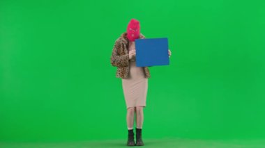 Pembe kar maskeli kadın, kaplan ceketli ve elinde mavi bayrak olan gece elbisesi. Stüdyoda yeşil arka plandaki ucube kadın. Moda eğilimi, feminist moda eğilimi