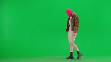 Pembe kar maskeli kadın, kaplan kürkü, gece elbisesi ve elinde sopayla kameraya tehditkar bir şekilde bakan bir kadın. Stüdyoda yeşil arka plandaki ucube kadın. Moda eğilimi konsepti