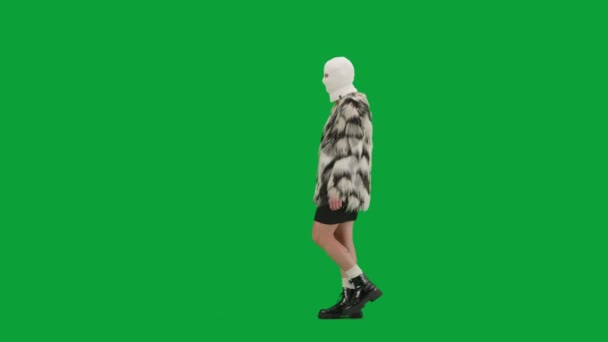 身穿白色巴拉克拉法帽 皮大衣和晚礼服的女人走路 工作室里的女性对绿色背景非常好奇 时尚潮流的概念 时尚方面的女性主义趋势 — 图库视频影像