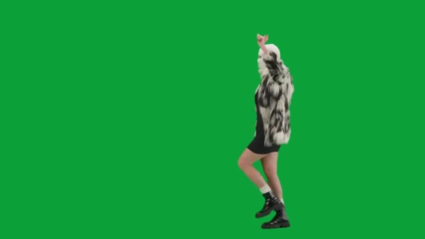 身穿白色巴拉克拉法帽 皮大衣和晚礼服的女人高兴地走着 手举着舞着 工作室里的女性对绿色背景非常好奇 时尚潮流的概念 — 图库视频影像