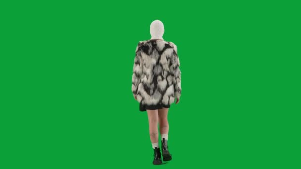 身穿白色巴拉克拉法帽 皮大衣和晚礼服的女人走路 工作室里的女性对绿色背景非常好奇 时尚潮流的概念 时尚后视镜中的女性主义趋势 — 图库视频影像