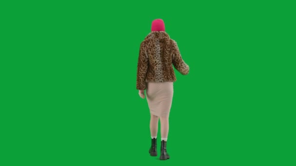 身穿粉色巴拉克拉瓦 虎皮大衣和晚礼服的女人走路 工作室里的女性对绿色背景非常好奇 时尚潮流的概念 时尚后视镜中的女性主义趋势 — 图库视频影像