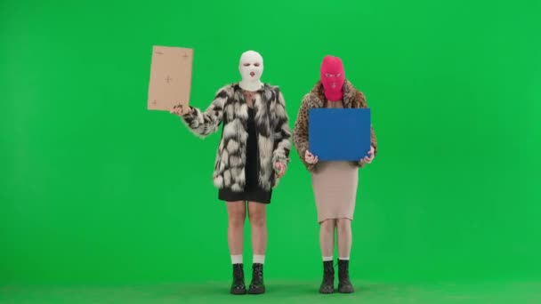 两名身穿巴拉克拉瓦和假皮毛外套的妇女在绿色屏幕上的工作室里纠察着 妇女指着手中的海报和标语牌高喊口号 — 图库视频影像