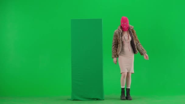 一个穿着粉色巴拉克拉瓦 虎皮大衣和衣服的女人从绿色横幅后面出来 用手指指指它 工作室里的女人都是绿色背景的时尚潮流概念 — 图库视频影像