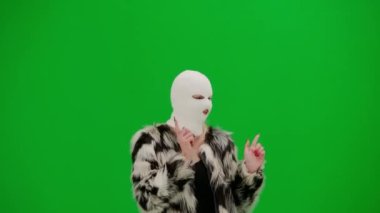Beyaz kar maskeli kadın, palto ve gece elbisesi giyen dans eden ve işaret parmağını farklı yönlere çeviren kadın. Stüdyoda yeşil geçmişi olan ucube kadın.