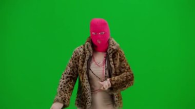 Pembe kar maskeli kadın, kaplan kürkü manto ve gece elbisesi giyip neşeyle dans ediyor. Stüdyoda yeşil arka plandaki kadın ucubesi. Moda eğilimi, feminist moda eğilimi