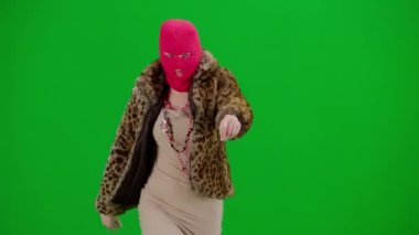 Pembe kar maskeli, kaplan kürklü ve gece elbisesi giymiş bir kadın dans edip zıplıyor. Stüdyoda yeşil arka plandaki ucube kadın. Moda eğilimleri kavramı, feminist moda eğilimi