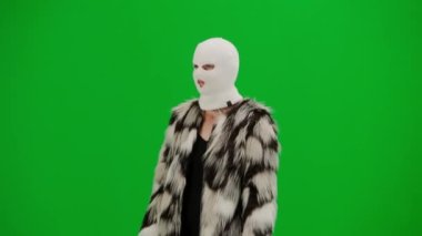 Beyaz kar maskeli kadın, kürk manto ve gece elbisesi yürüyüşü. Stüdyoda yeşil arka plandaki kadın ucubesi. Moda eğilimi, feminist moda eğilimi Yarım dönüş.