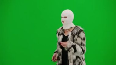 Beyaz kar maskeli kadın, palto ve gece elbisesi giyiyor. Stüdyoda yeşil arka plandaki ucube kadın. Moda eğilimleri, feminist moda eğilimi Yarım dönüş.