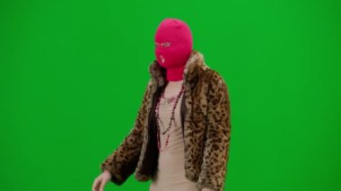 Pembe kar maskeli kadın, kaplan kürkü manto ve gece elbisesi yürüyüşü. Stüdyoda yeşil arka plandaki kadın ucubesi. Moda eğilimi, feminist moda eğilimi Yarım dönüş.