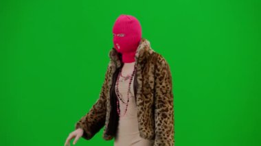 Pembe kar maskeli kadın, kaplan kürkü manto ve gece elbisesi yürüyüşü. Stüdyoda yeşil arka plandaki kadın ucubesi. Moda eğilimi, feminist moda eğilimi Yarım dönüş.