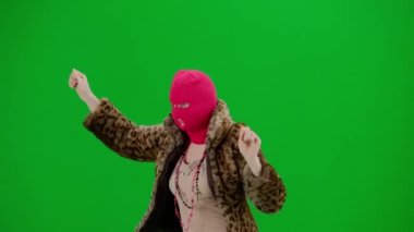 Pembe kar maskeli bir kadın, kaplan kürkü bir ceket ve elleri havada neşeyle yürüyüp dans eden bir elbise. Stüdyoda yeşil arka plandaki kadın ucubesi. Moda eğilimi, feminist moda eğilimi Yarım dönüş.