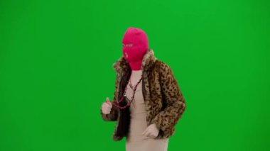 Pembe kar maskeli kadın, kaplan ceketli ve gece elbisesi giymiş. Stüdyoda yeşil arka plandaki ucube kadın. Moda eğilimleri, feminist moda eğilimi Yarım dönüş.