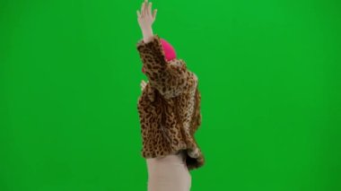 Pembe kar maskeli bir kadın, kaplan kürkü bir ceket ve elleri havada neşeyle yürüyüp dans eden bir elbise. Stüdyoda yeşil arka plandaki kadın ucubesi. Moda eğilimi kavramı, feminist moda eğilimi